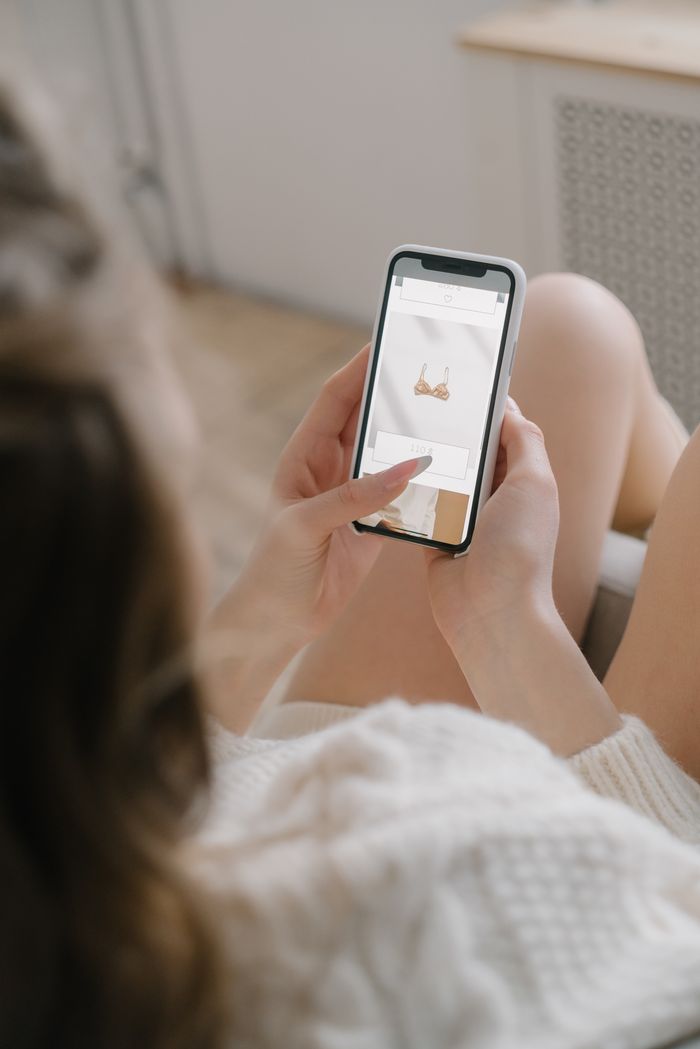 A woman browses an online store while relaxing indoors, using her smartphone with focus on shopping.